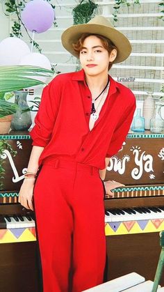 a young man in a red jumpsuit and hat standing next to a piano