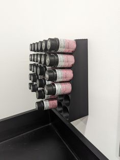 there is a black shelf with pink and silver cups on it in front of a white wall