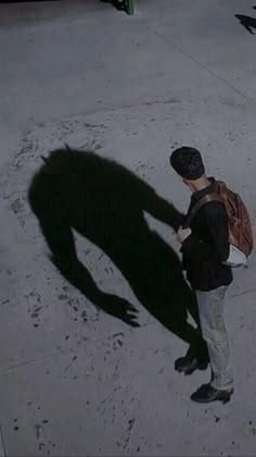 a man with a backpack standing on the sidewalk looking at his cell phone and casting a long shadow