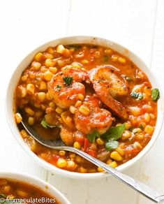 two bowls of shrimp and corn soup with a spoon in them on a white surface