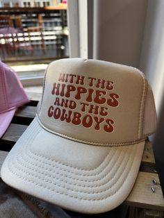 Tab trucker hat that says, "With the hippies and the cowboys". Retro Summer Trucker Hat With Wide Brim, Vintage Adjustable Baseball Cap For Rodeo, Retro Wide Brim Trucker Hat For Summer, Retro Summer Trucker Hat For Rodeo, Vintage Trucker Hat For Country Events, Vintage Trucker Hat For Rodeo, Vintage Style Trucker Hat For Rodeo, Adjustable Vintage Snapback Hat For Rodeo, Vintage Adjustable Trucker Hat With Letter Print