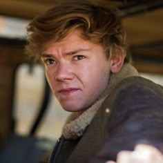 a close up of a person wearing a jacket and holding something in his hand while looking at the camera