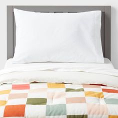 an unmade bed with white sheets and colorful checkered bedspread on it