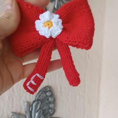 a hand holding a red knitted bow with white flowers