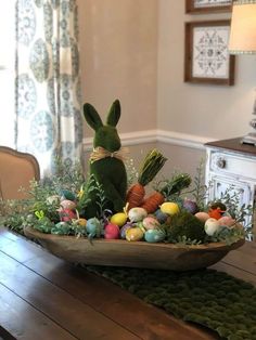 a wooden table topped with an easter basket filled with eggs and grass next to a window