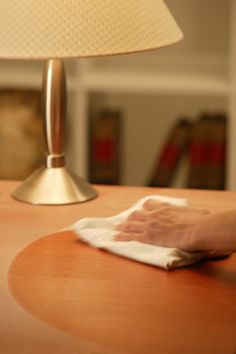 a person wiping up with a cloth on a table next to a lamp and bookshelf