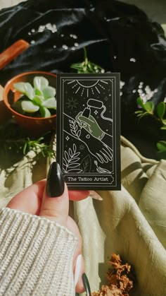 a person holding up a tarot card in front of some plants and food on a blanket