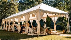 a group of people sitting under a white tent in the middle of a field with trees