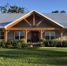 a house that is in the grass with a blue roof and some bushes around it