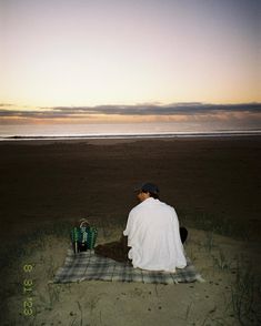 a man sitting on top of a blanket near the ocean