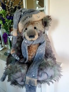 a teddy bear wearing a hat and scarf on top of a dresser next to flowers