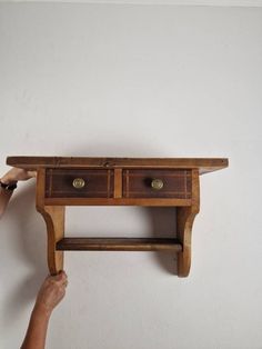 a person holding up a wooden shelf with two drawers on each side and one drawer at the top