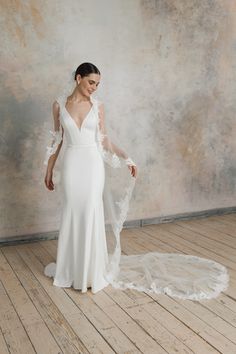 a woman in a white wedding dress standing on a wooden floor with her veil draped over her shoulder