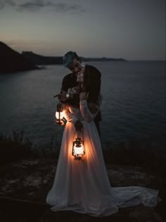 a bride and groom kissing in front of the ocean with lanterns lit up at night