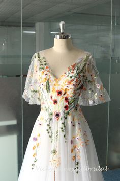 a white dress with flowers on it is displayed in front of a glass display case