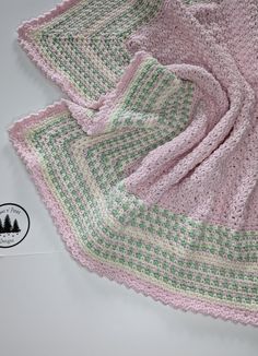 a pink and green crocheted blanket laying on top of a white tablecloth