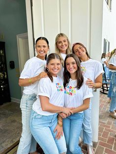 four girls in white shirts and jeans posing for the camera with their arms around each other