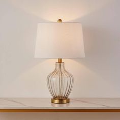 a table lamp with a white shade on it and a gold frame around the base