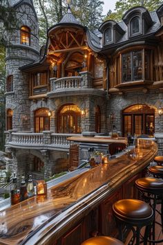 an outdoor bar with lots of stools next to a stone castle like building in the woods