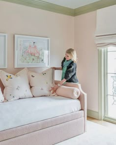 a woman standing next to a couch in a living room with pink walls and furniture