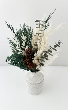 a white vase filled with lots of different types of flowers and greenery on top of a table