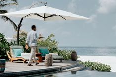 a man walking on a deck next to an umbrella over the pool and lounge chairs