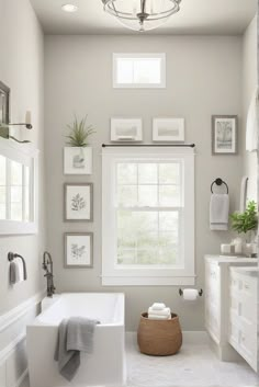 a white bathroom with pictures on the wall and a bathtub in front of a window