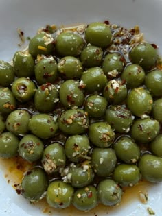 some green olives are in a white bowl with brown stuff on top and sprinkled