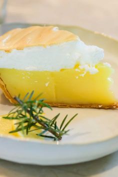 a slice of lemon pie on a plate with a sprig of rosemary next to it