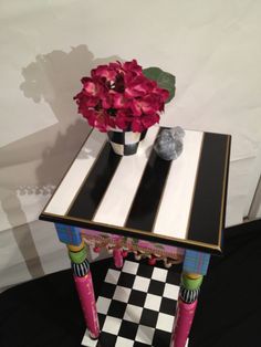 a black and white checkerboard table with flowers on the top, next to a potted plant