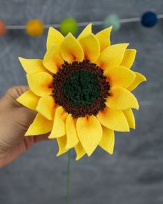 a hand holding a fake yellow sunflower with green center