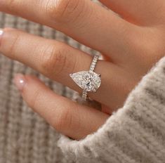 a woman's hand with a diamond ring on top of her finger, wearing a sweater