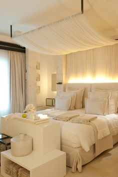 a large white bed sitting in a bedroom next to a tall glass table with flowers on it