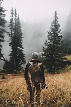 a man with a backpack is walking through the foggy woods on a trail in the mountains