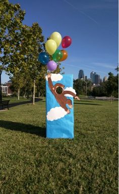 a paper bag with balloons attached to it in the grass