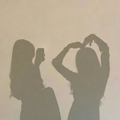 two women standing next to each other in front of a white wall with the shadow of their hands