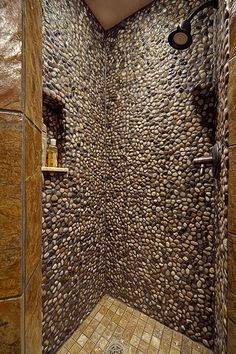 a walk in shower with rocks on the wall and tile flooring next to it