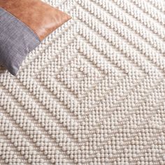 a pillow on top of a white rug with brown leather accents and a tan cushion