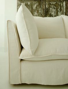 a white couch with pillows on it in front of a wooden wall and window frame