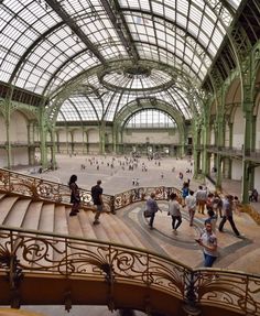 many people are walking around in an indoor area with high ceilings and glass windows on the ceiling