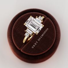 an engagement ring with three baguettes on it in a velvet case, sitting on top of a white surface