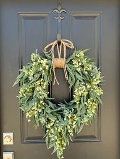 a wreath is hanging on the front door with green leaves and white flowers around it