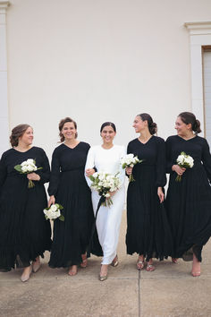 a group of women standing next to each other wearing black dresses and holding bouquets