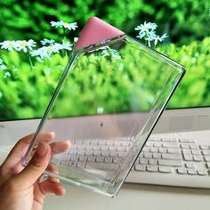 a hand holding a pink object in front of a computer screen with flowers on it