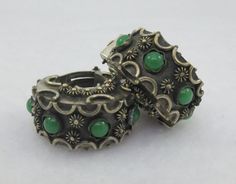 two rings with green stones on them sitting on a white surface, one is open and the other is closed