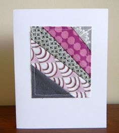 a white card with pink, grey and black designs on the front is sitting on a wooden table