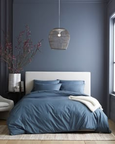 a bed with blue sheets and pillows next to a window in a room that has gray walls