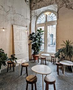 several tables and chairs in a room with large plants on the wall behind them, along with an arched window