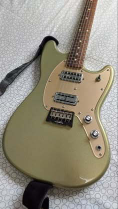 a green electric guitar laying on top of a white bed sheet with a black cord attached to it