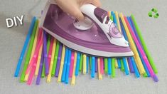 a person is ironing colored straws with a purple and white electric iron on top